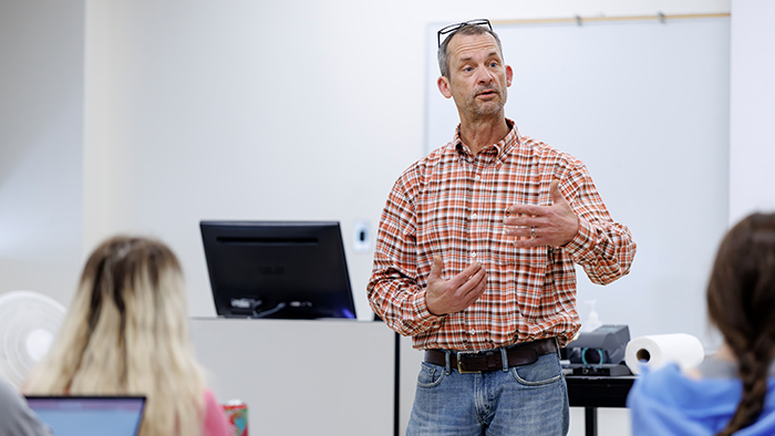 Man in plaid shirt teaching in a classroom.