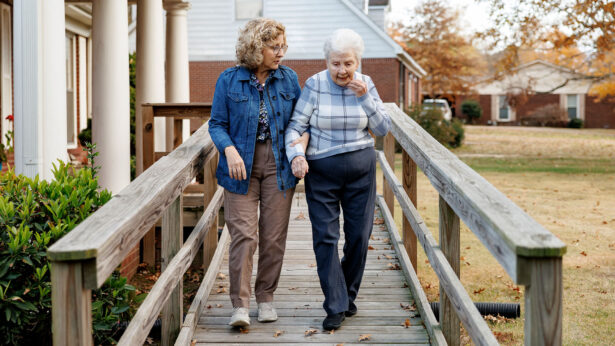 A women assisting an elderly woman walking down a wooden ramp.