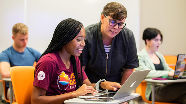 Female instructor helping a black female student working on a laptop.
