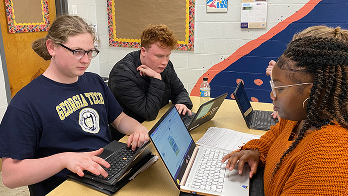 Three students sitting around a table using laptops.