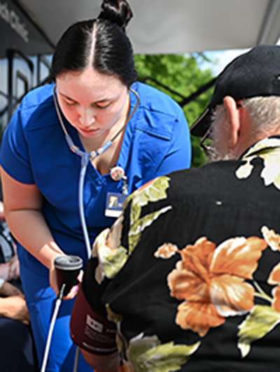 Female in blue scrubs takes a blood pressure reading from a man in a Hawaiian shirt.