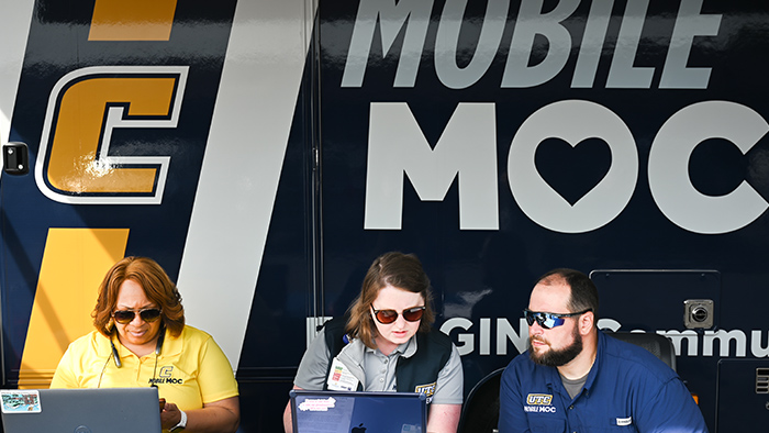 Three people in sunglasses sitting in front of a mobile health van.