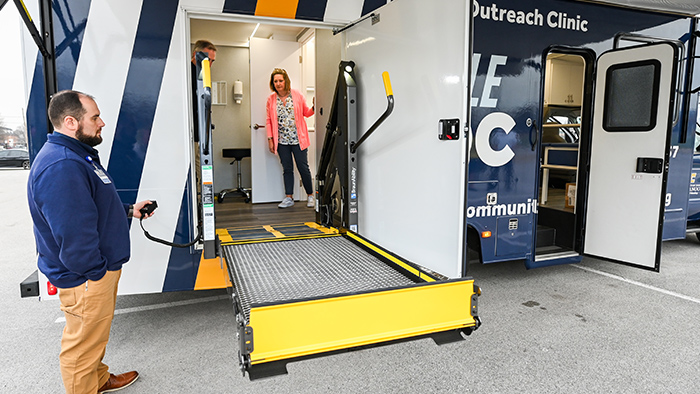 Three people examine the wheelchair access ramp of a mobile health clinic.
