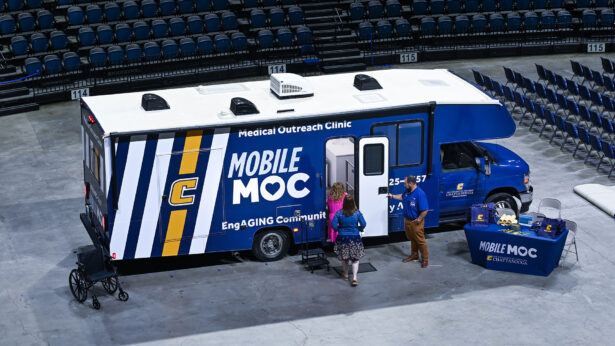 Three people exploring a blue mobile health clinic vehicle.