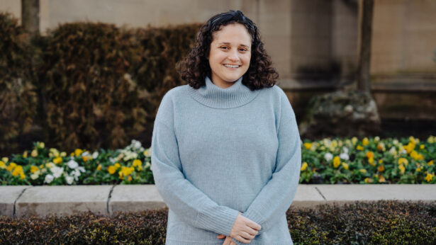 A woman with curly brown hair, wearing a gray sweater outside.