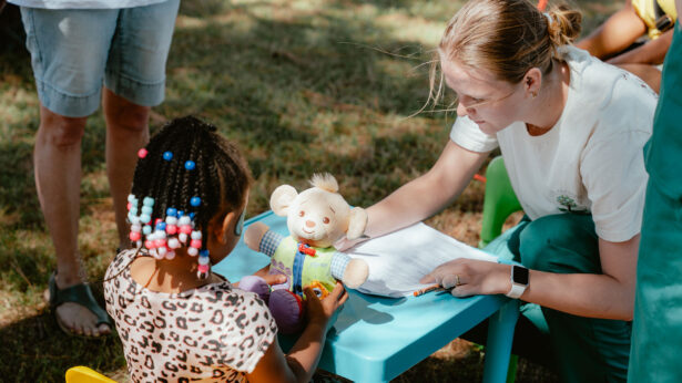 Female college student playing with a small black child outside.