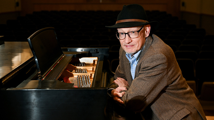 An older man posing next to a piano.