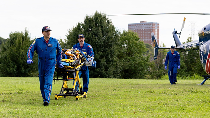 Two medical personnel wheel a gurney away from a landed helicopter.
