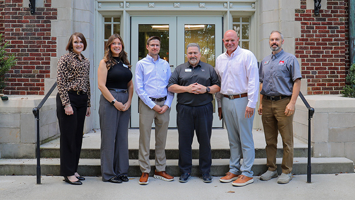 A group of six people posing for a photo outside a brick building.