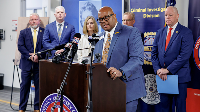 A man speaking from behind a podium, with a group of officials lined up behind him.