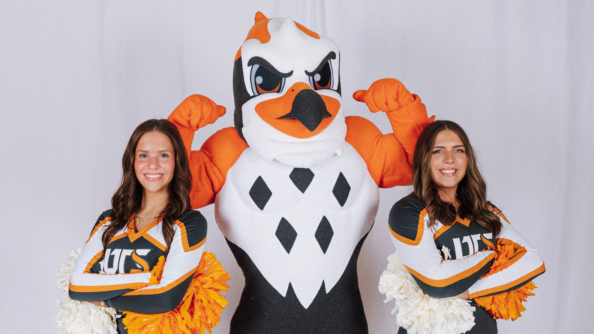 A bird mascot posing with two female cheerleaders.