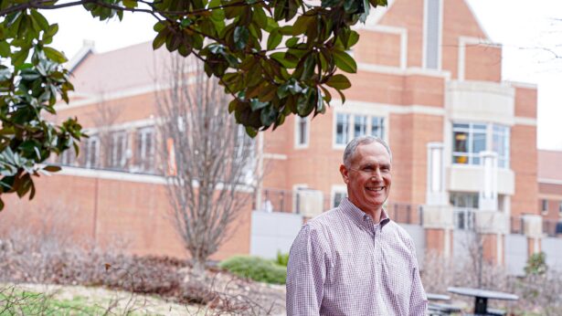 Man standing under a tree, in front of a building.