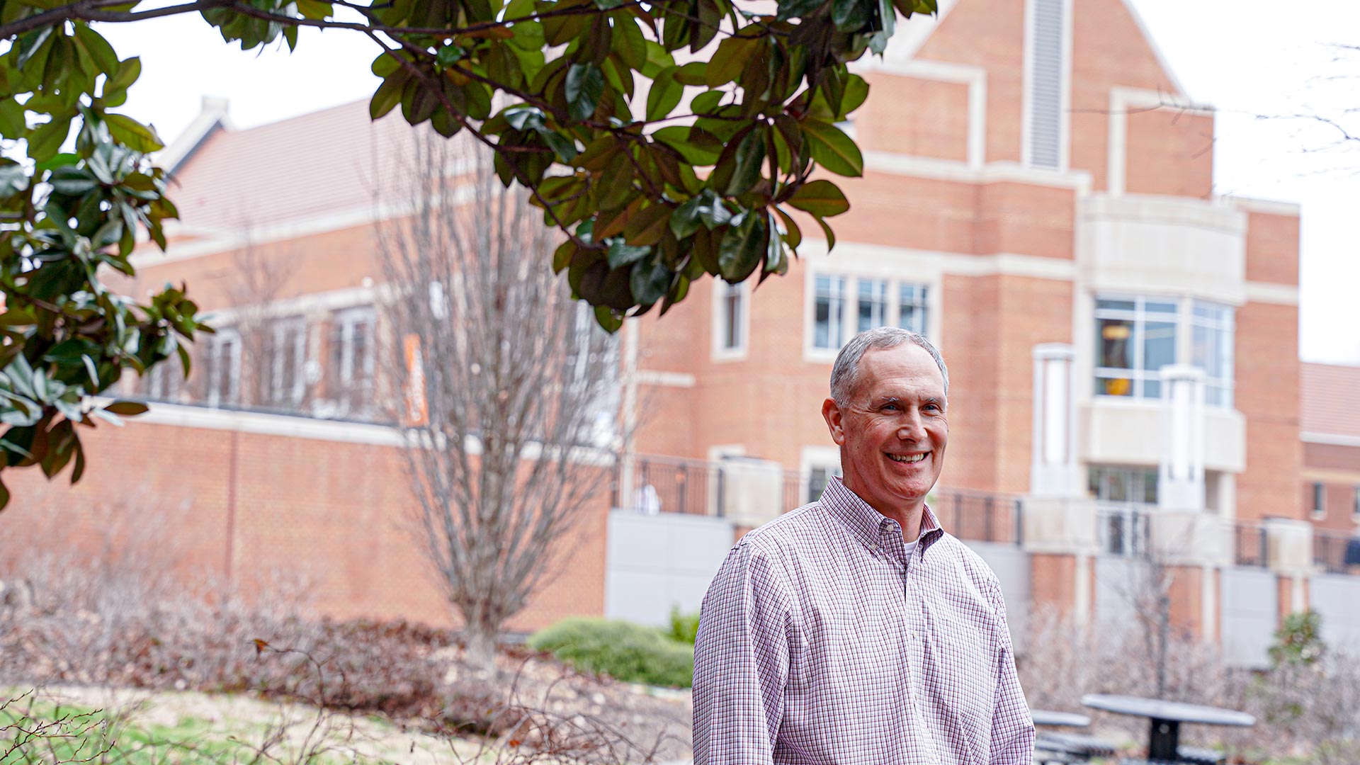 Man standing under a tree, in front of a building.
