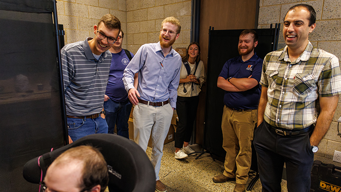 A group of people watching another person demonstrate using a piece of technology.