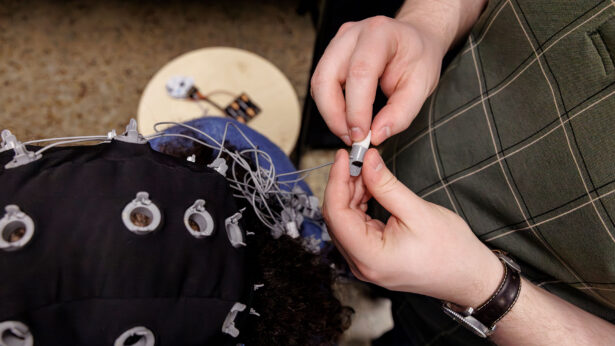 A person connects electrical sensors to a head-worn rig to measure brain activity.