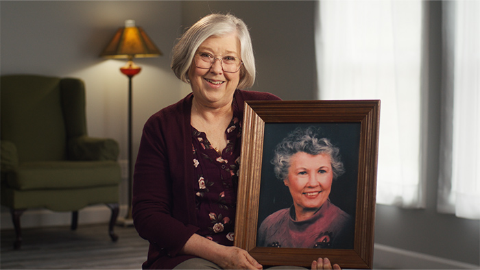 A woman sitting, holding a framed photo of another elderly woman.