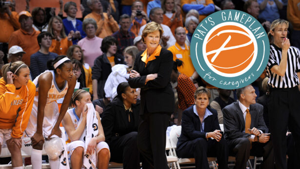 A basketball team and coaches on the sidelines, with a crowded stadium behind them.