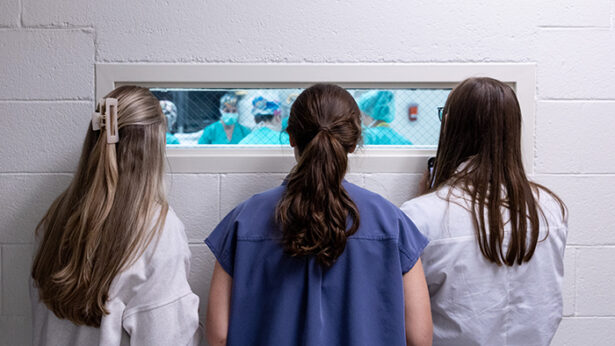 Three women looking through a window into an operating room.