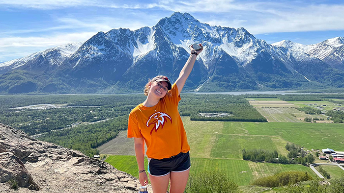 A young woman posing for a photo with a snow-capped mountain range in the background.