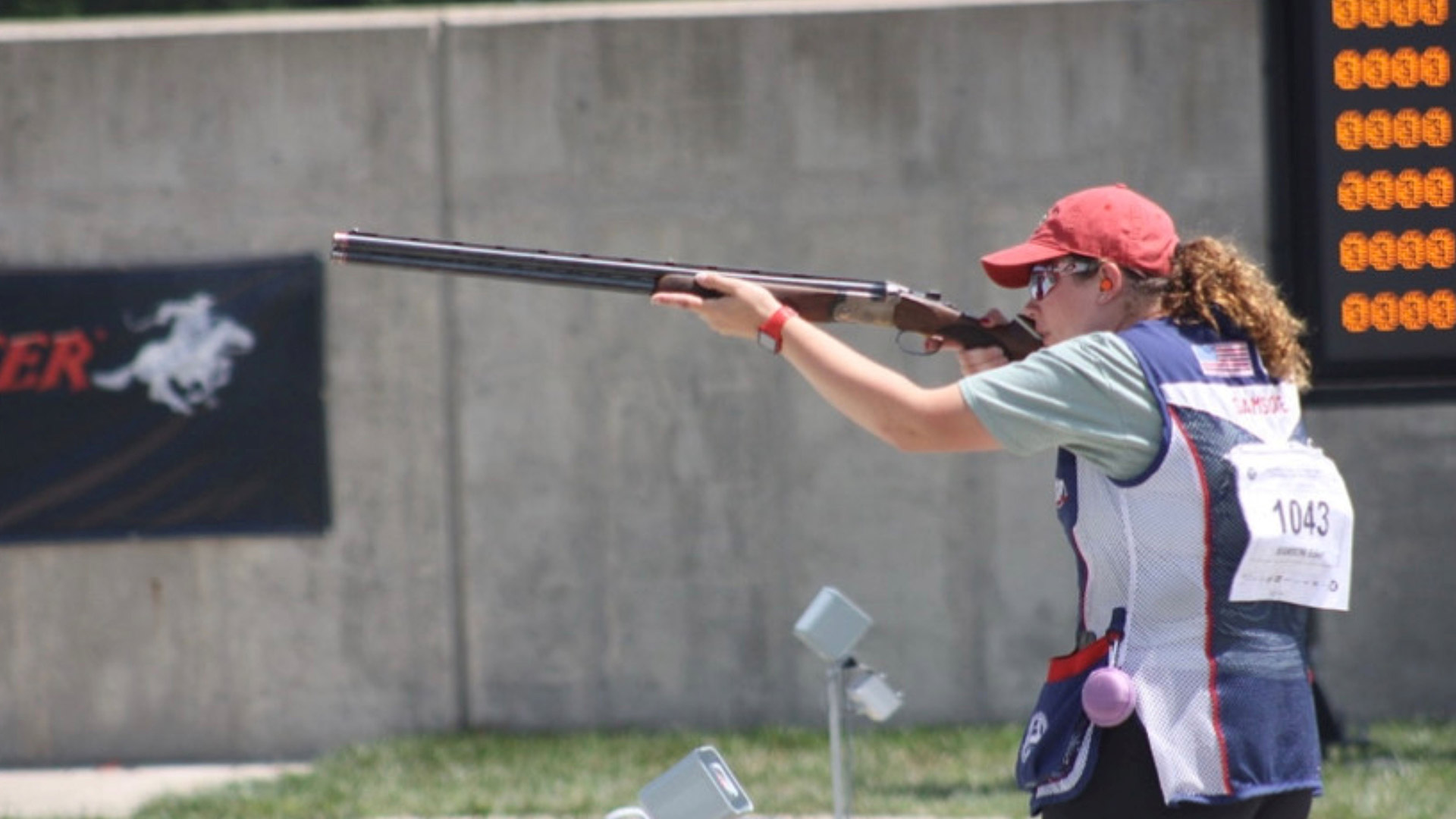 A woman aiming a shotgun at a target range.