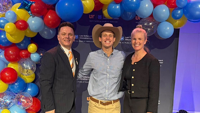 Three people smiling for a photo against an event backdrop.