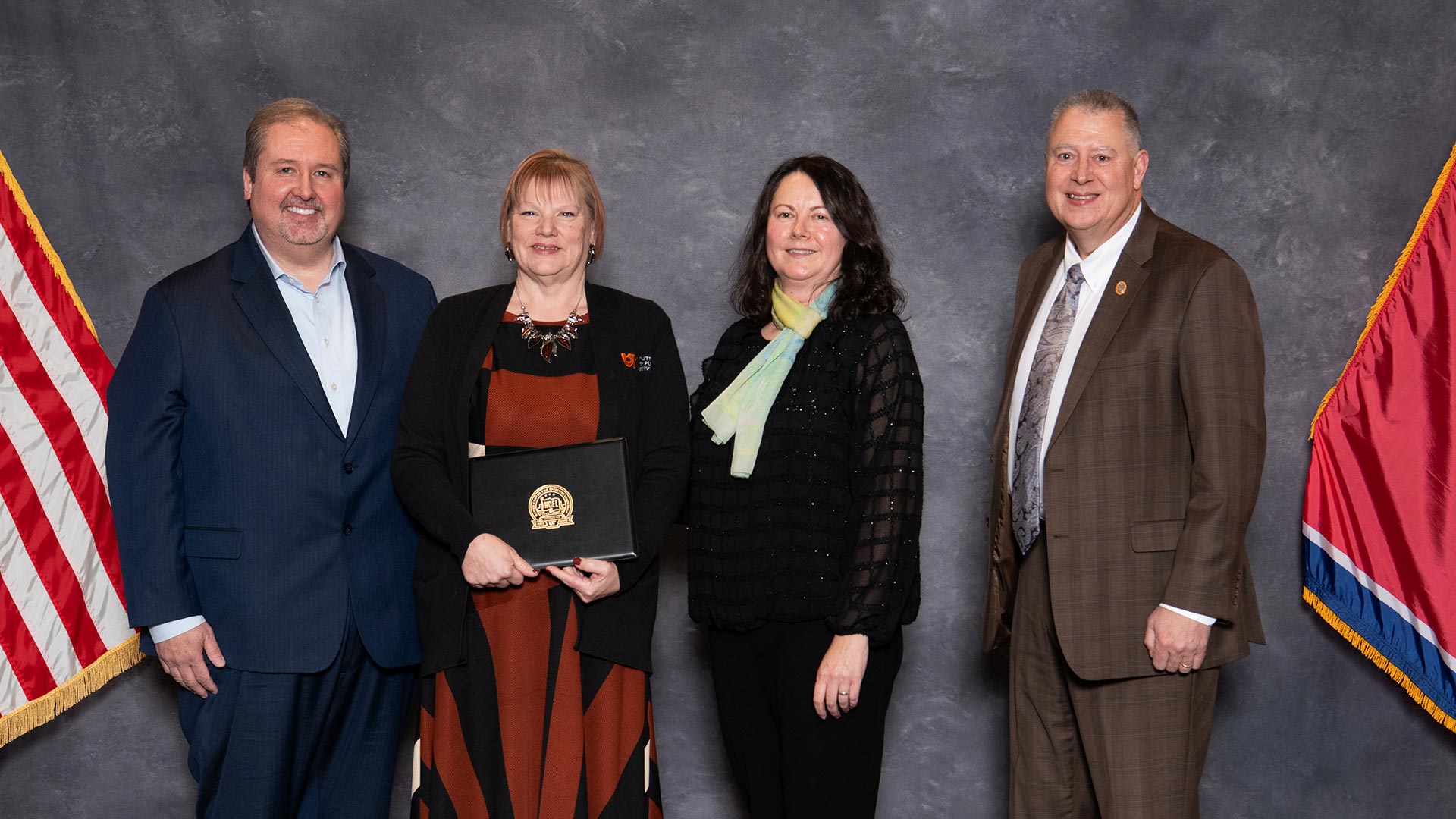 Four people posing for a group photo with the Tennessee flag and the U.S. flag.