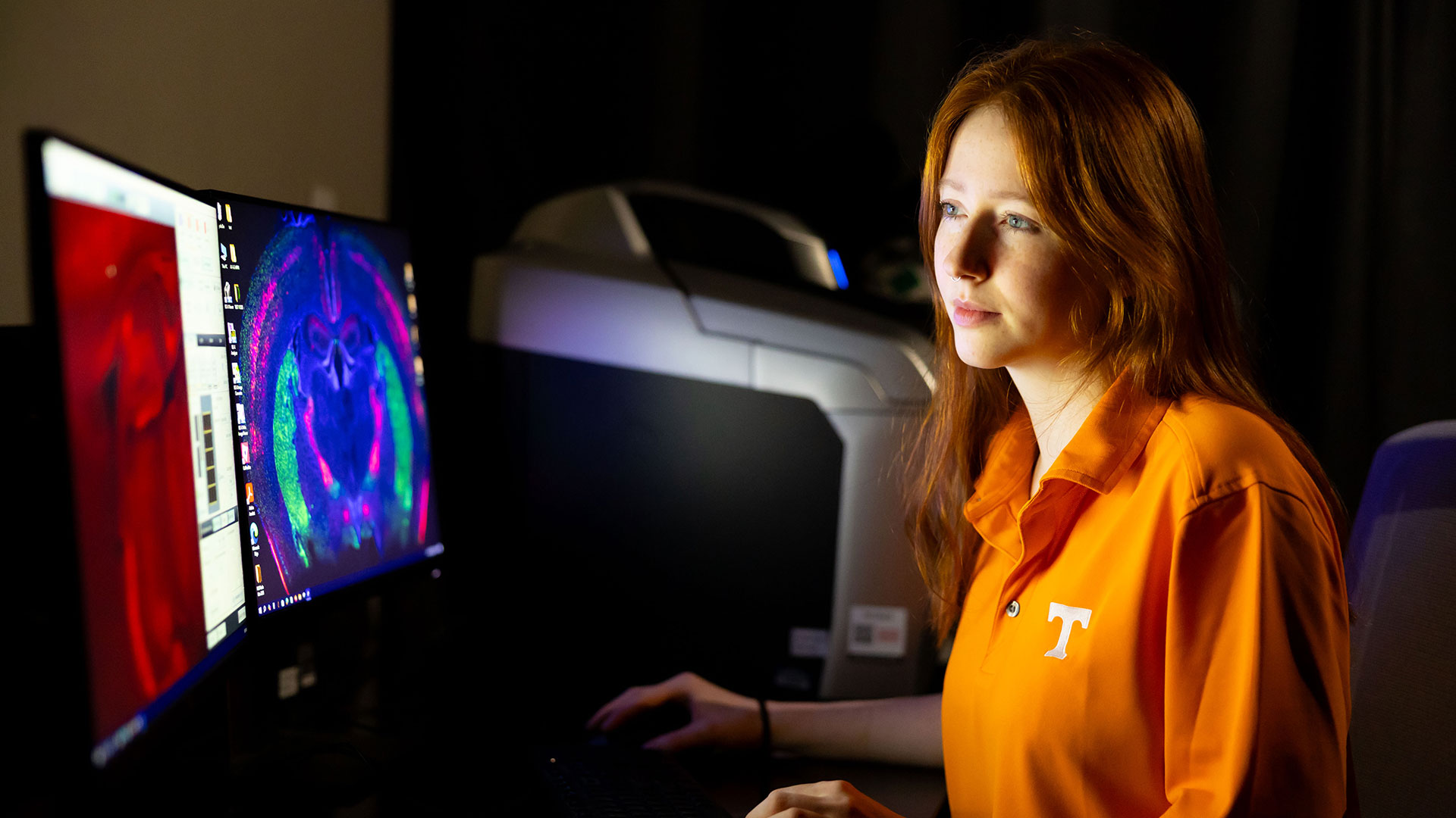 A woman in an orange shirt examining a computer screen readout.