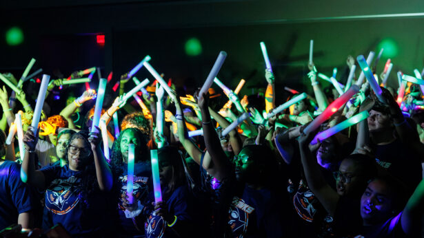 A group of students waving glow sticks in a dark party room.