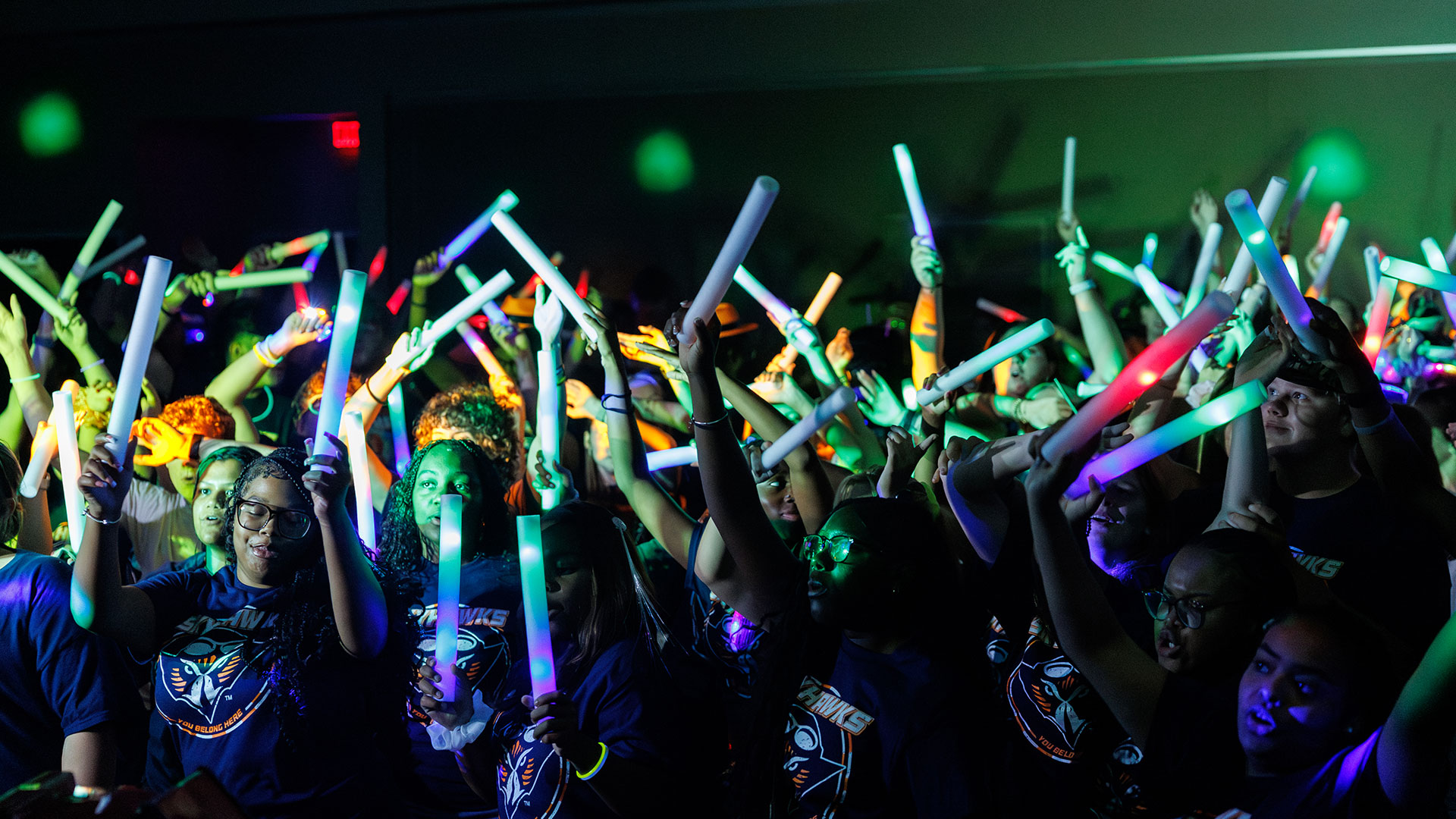 A group of students waving glow sticks in a dark party room.