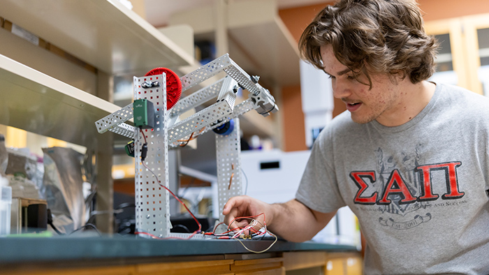 A young man working on some wires in a lab.