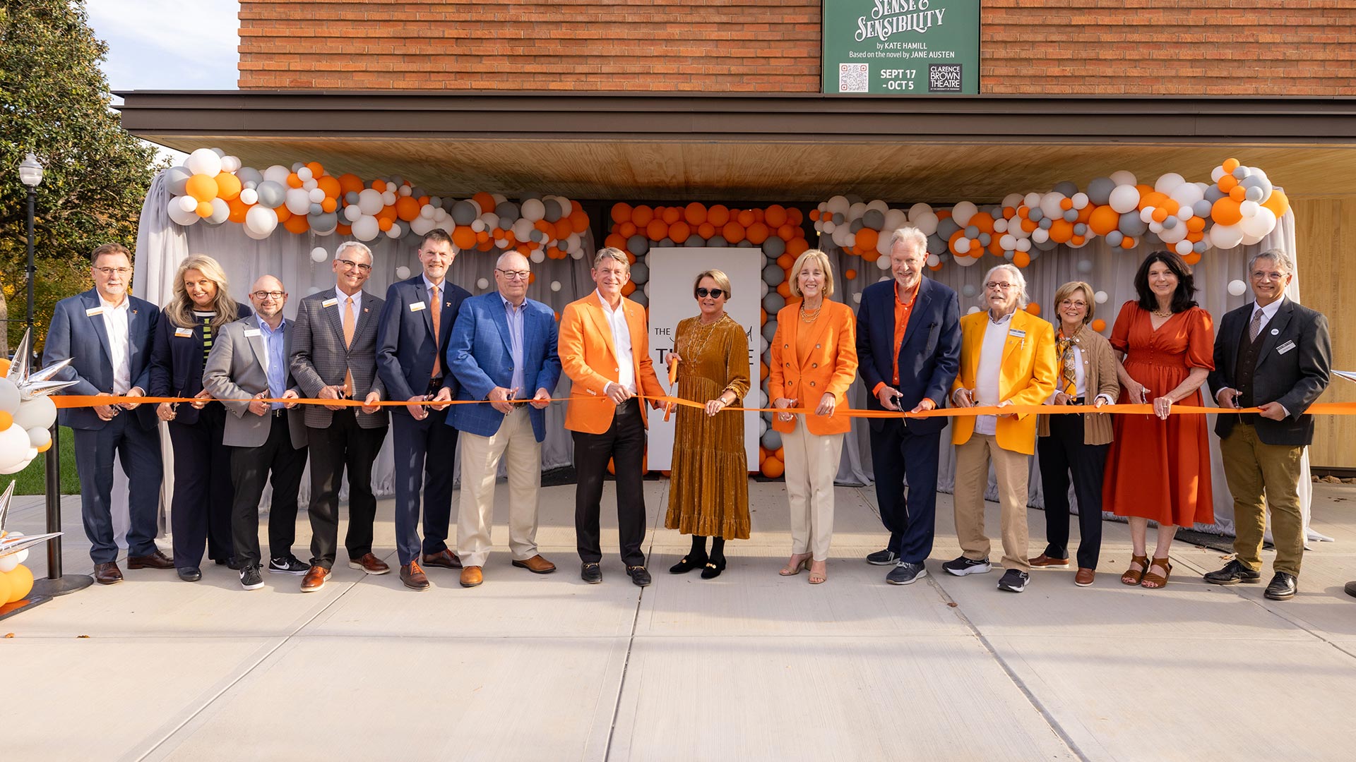 A line of people holding an orange ribbon during a ribbon cutting ceremony.