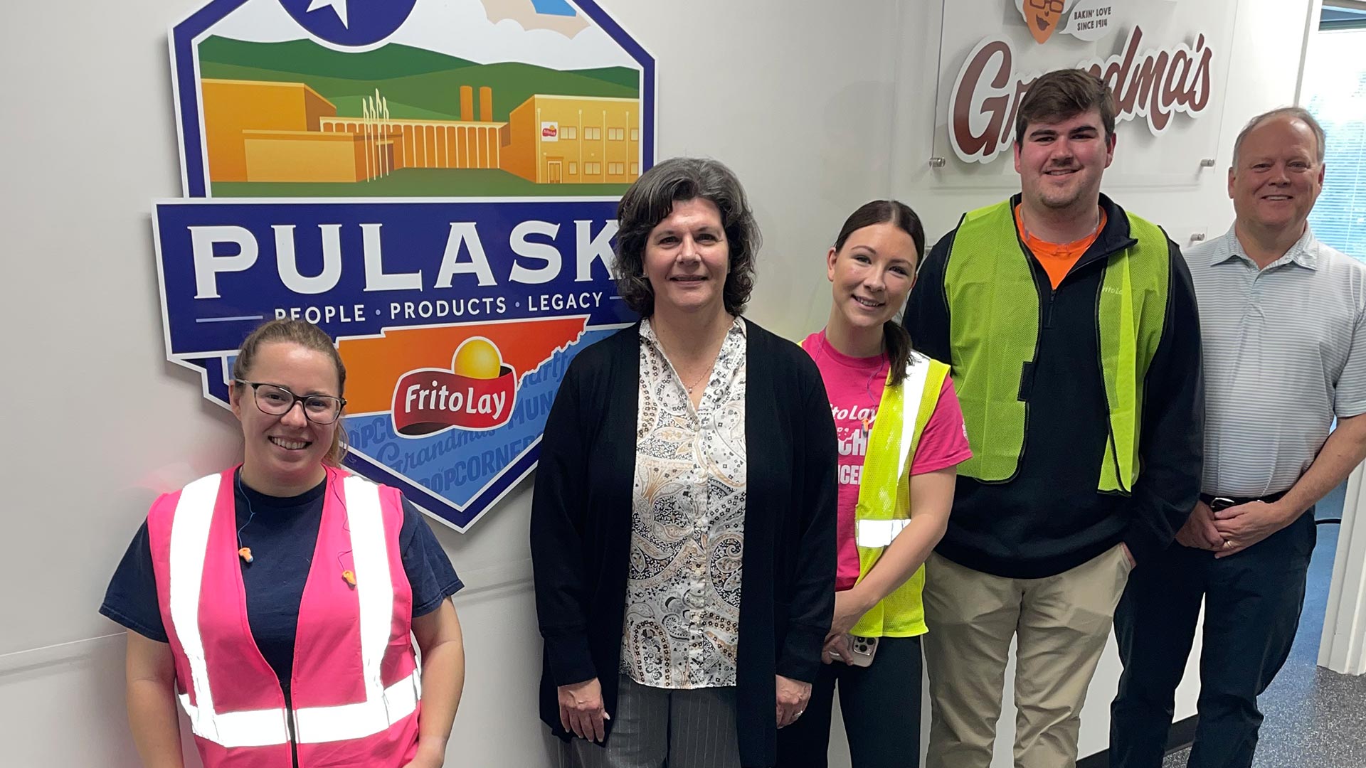 A group of smiling people lined up next to a sign that says "Pulaski. People. Products. Legacy."