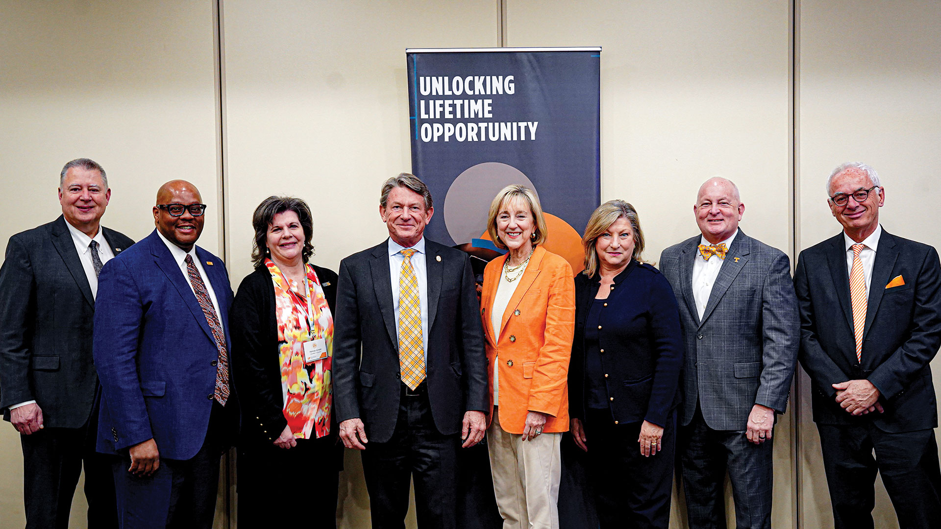 A group of men and women standing in front of a pull-up banner which says "Unlocking Lifetime Opportunity."