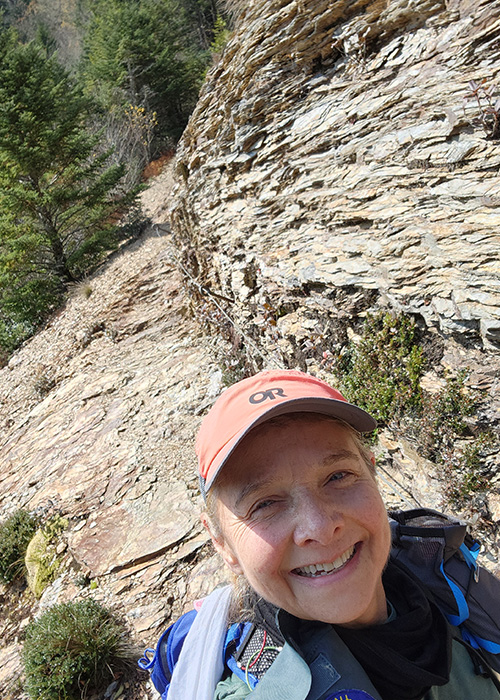 A woman taking a selfie along a rocky trail in the mountains.