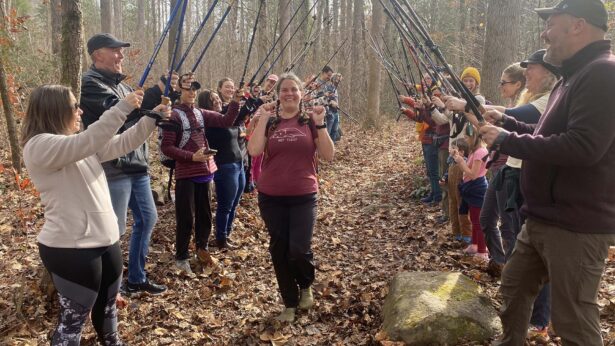 A woman walks between two lines of hikers holding up their walking sticks as an archway.