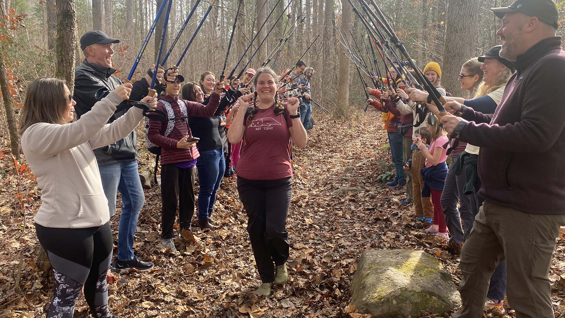 A woman walks between two lines of hikers holding up their walking sticks as an archway.
