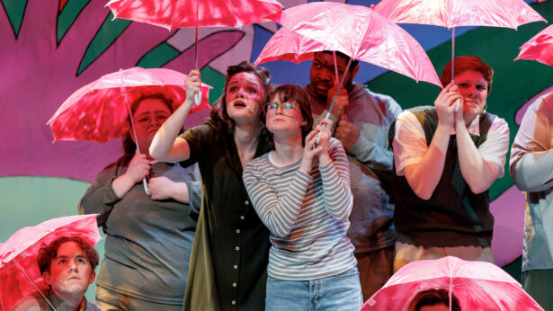 A group of student actors putting on a show, all holding pink umbrellas.