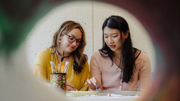 Two girls painting together on a canvas.