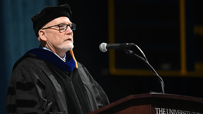 Man in commencement regalia speaking at a podium.