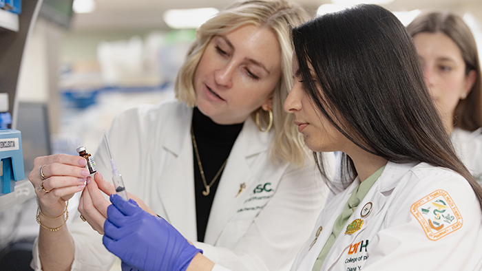 Two women in lab coats examining a vial and syringe.