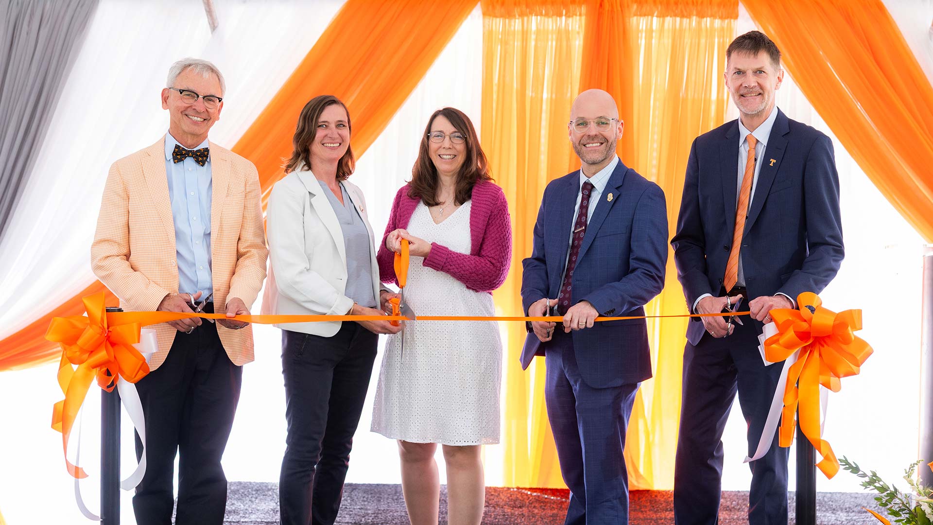 A group of five people preparing to collectively cut a ceremony ribbon.