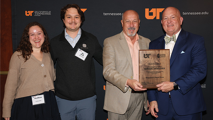 Four people standing for a photo while holding a wooden award plaque.