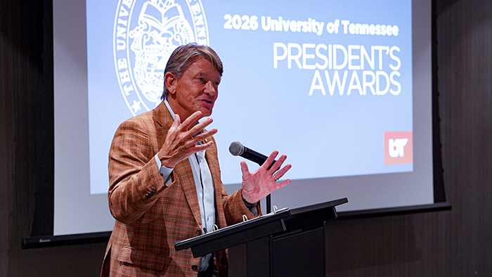 A man talking from behind a podium, with a presentation screen in the background.