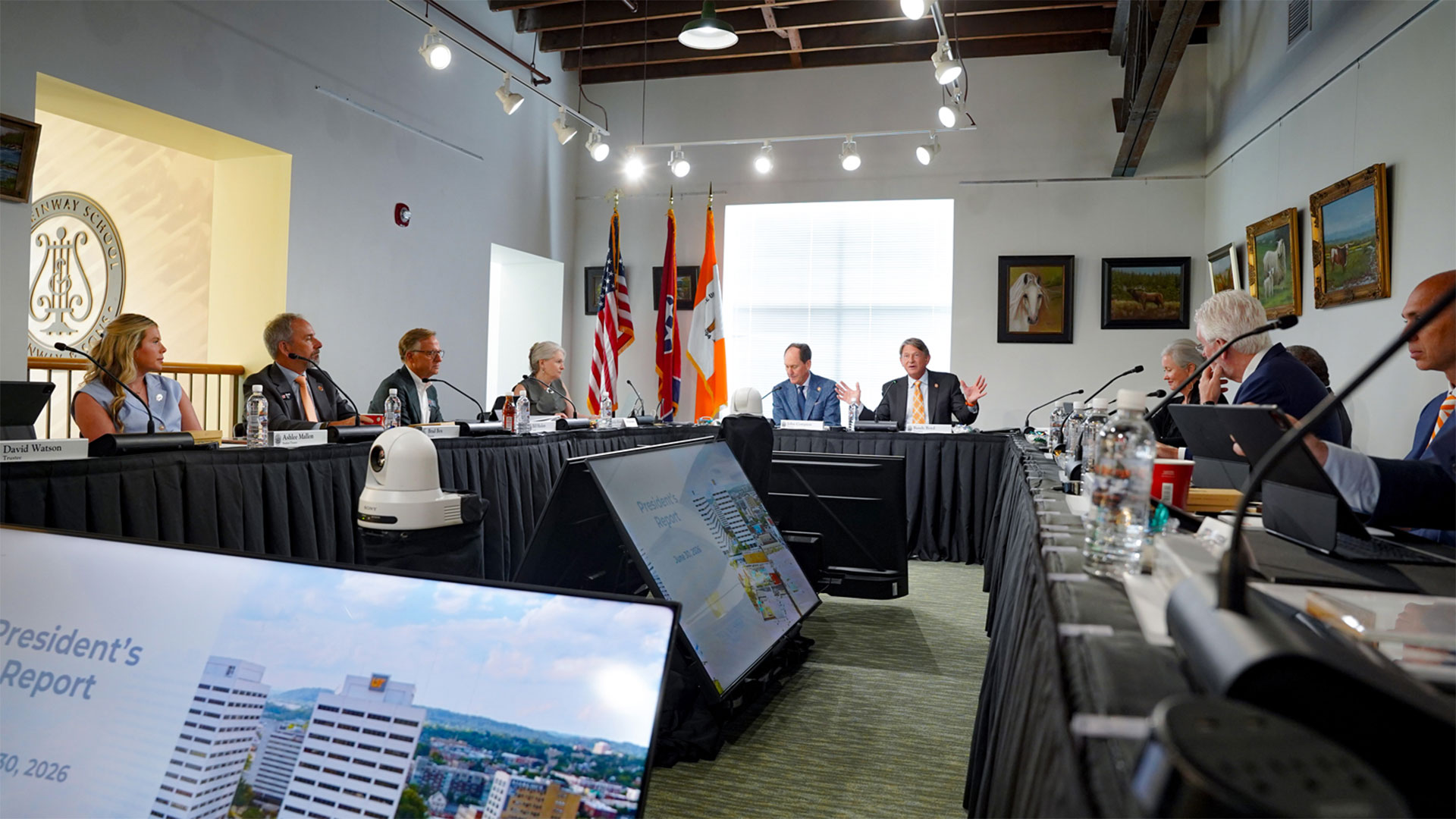 A group of executives meeting while sitting at conference tables, each with name placards and microphones.