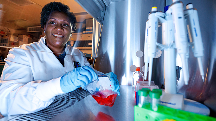 Woman holding a bottle of red liquid inside a laboratory workbench.