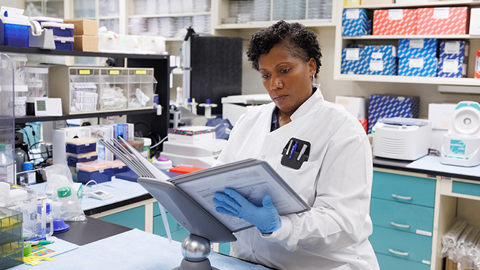 Woman in a lab coat reading a binder while sitting in a laboratory.
