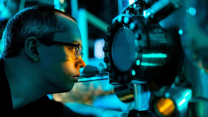 A man closely examines an experiment through a small window in a large piece of equipment.