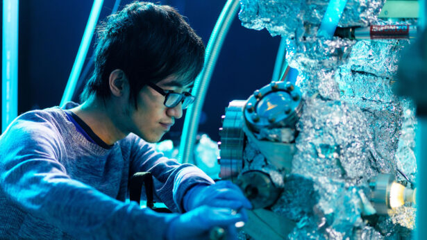 A man closely examines an experiment through a small window in a large piece of equipment.