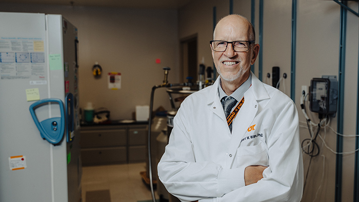 Bald man in a white lab coat, standing in a laboratory space.