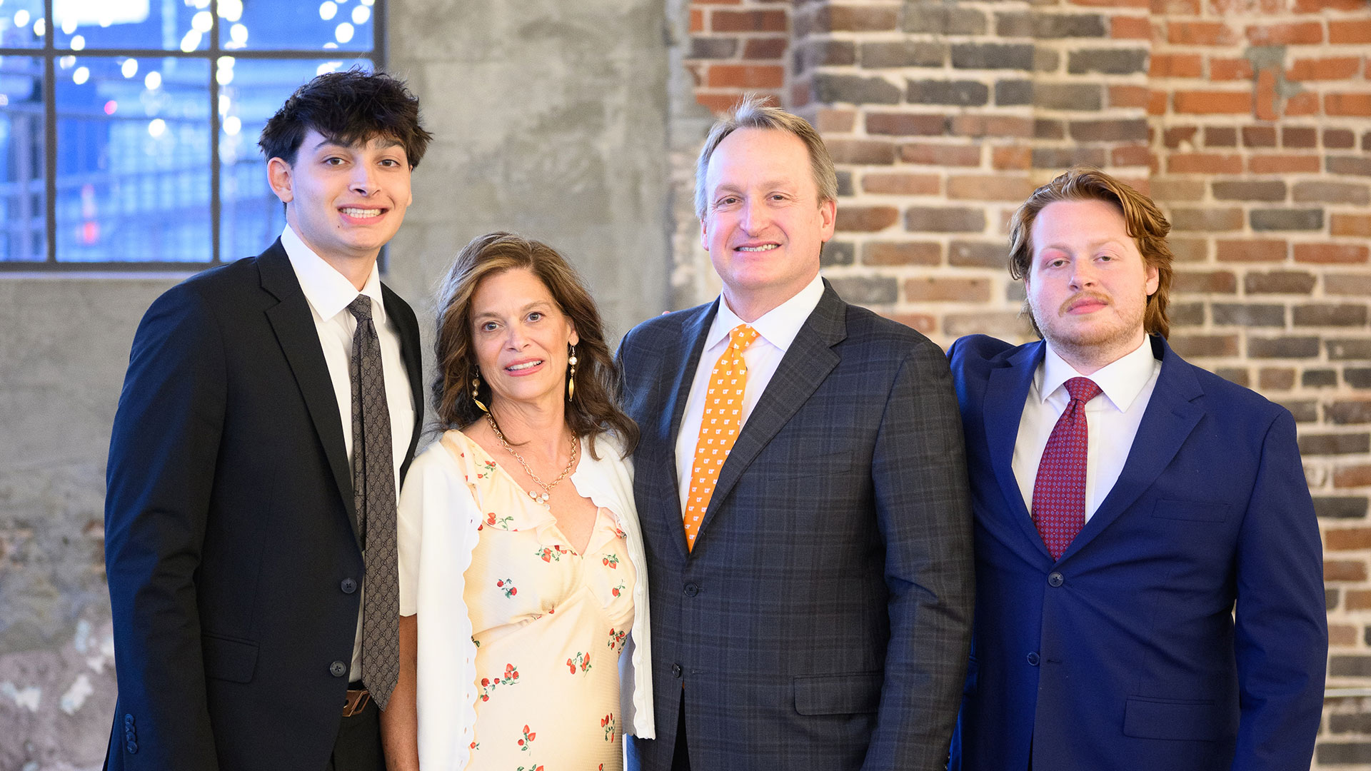 A man and wife pose for a family photo with their two adult sons.